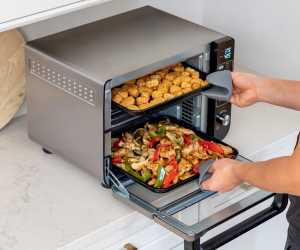 Someone pulling chicken nuggets and chicken and peppers out of the Ninja 12-in-1 Double Oven