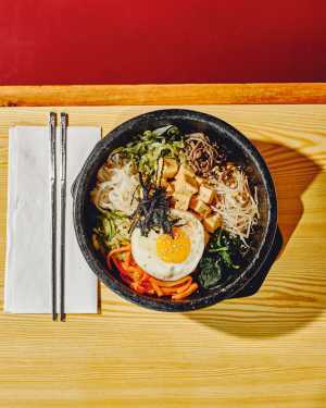 Korean Village | Fried tofu bibimbap is served in a sizzling hot stone bowl with seasoned rice and veggies, and topped with an egg