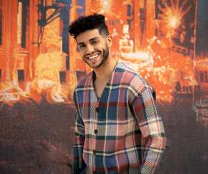 Mena Massoud | Mena Massoud, Aladdin actor smiling at the camera in front of a colourful wall