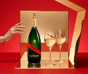 GH Mumm | A hand reaches for a bottle of GH Mumm which sits beside two champagne glasses on a red background