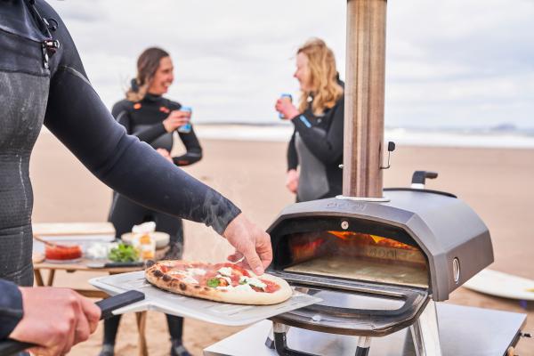 Taking a pizza out of the Ooni Karu 12G pizza oven at the beach