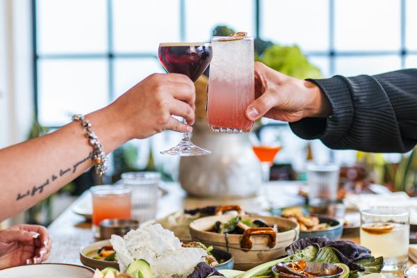 Best Thai restaurants in Toronto | Two people cheers cocktails over a spread of dishes at Favorites Thai BBQ