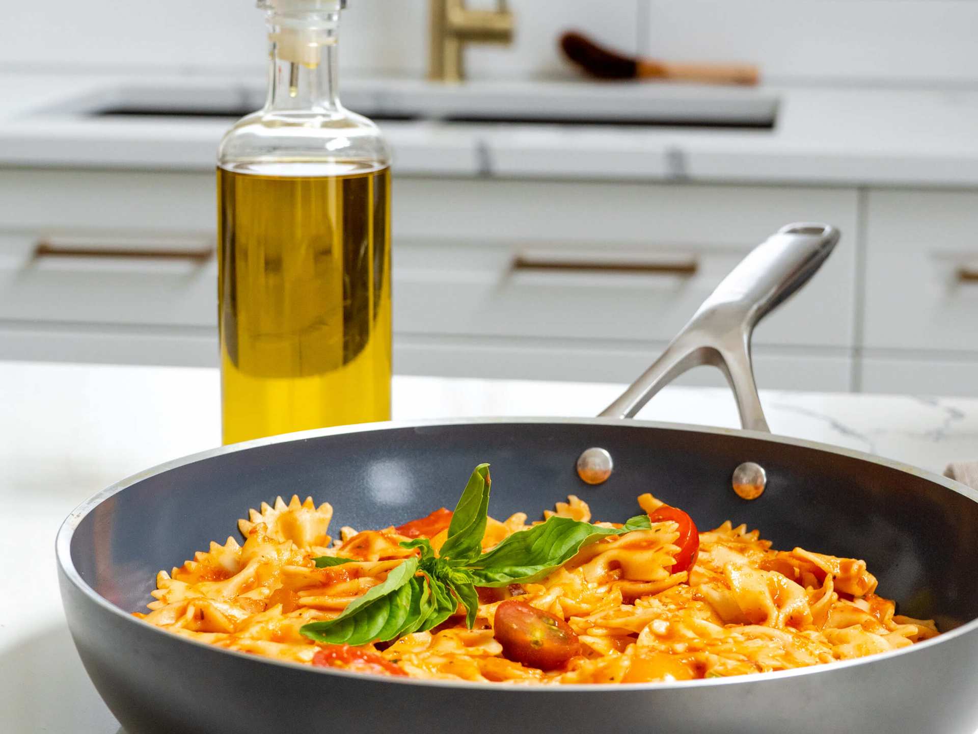 Kilne Everything Pan with ribbon pasta and a bottle of olive oil on a kitchen counter