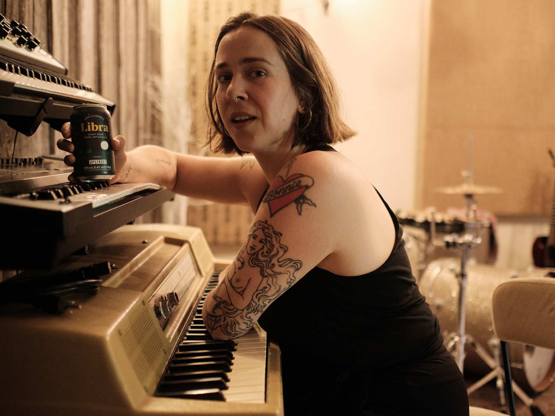 Serena Ryder leaning on her piano with a can of Libra non-alcoholic craft beer