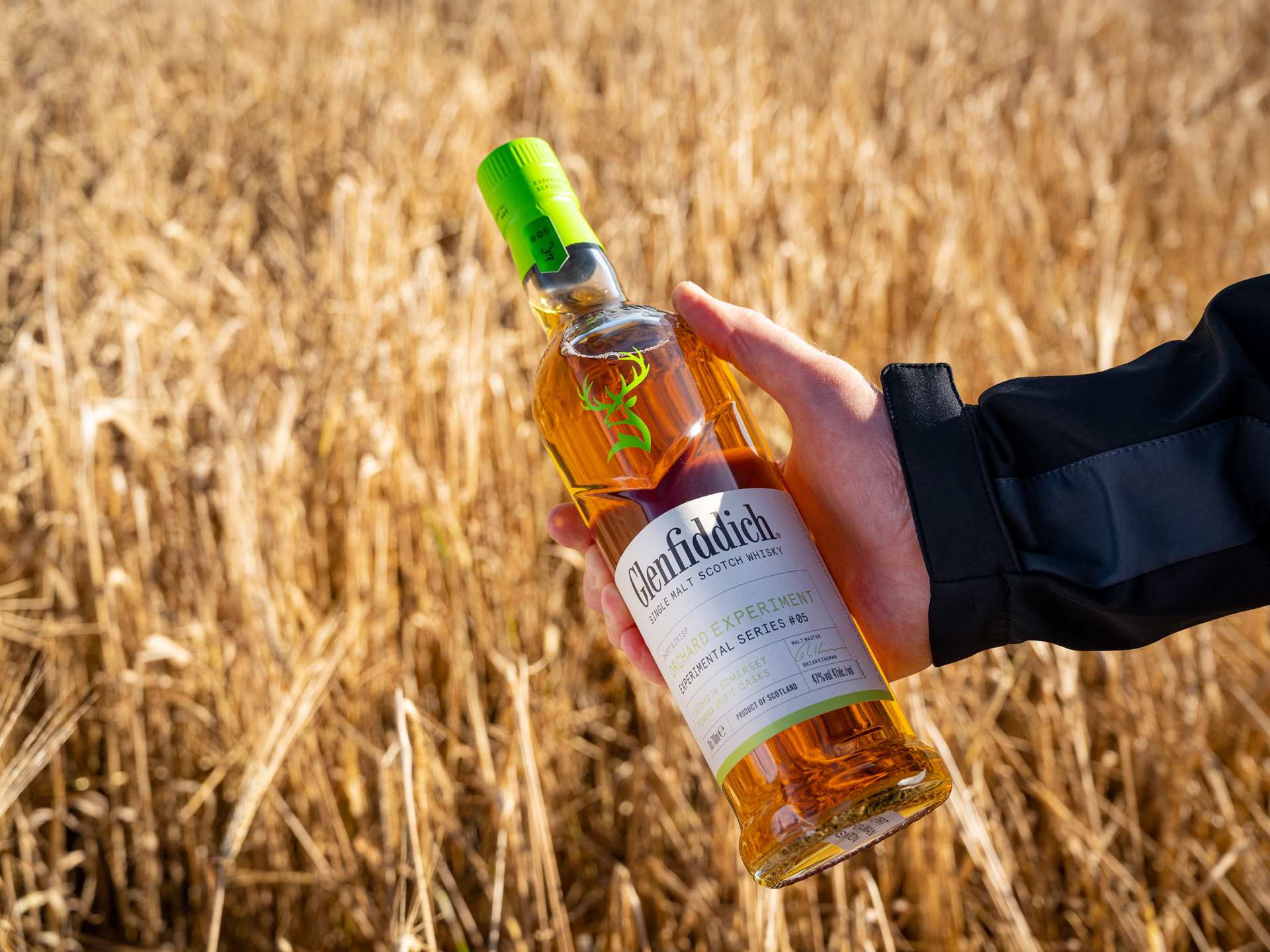 Glenfiddich The Orchard Experiment | A hand holds a bottle of The Orchard Experiment in a field