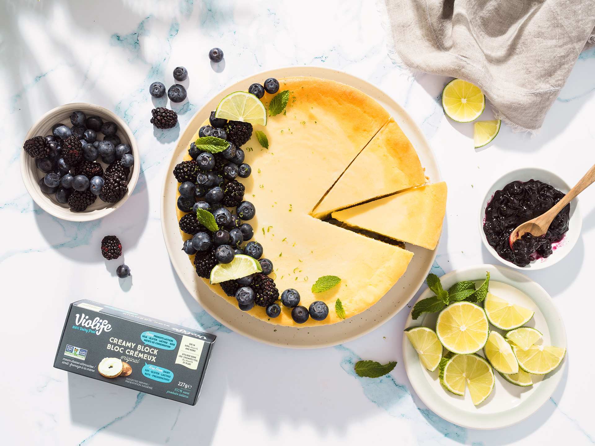 An overhead view of a cheesecake topped with blueberries, and a Violife Creamy Block