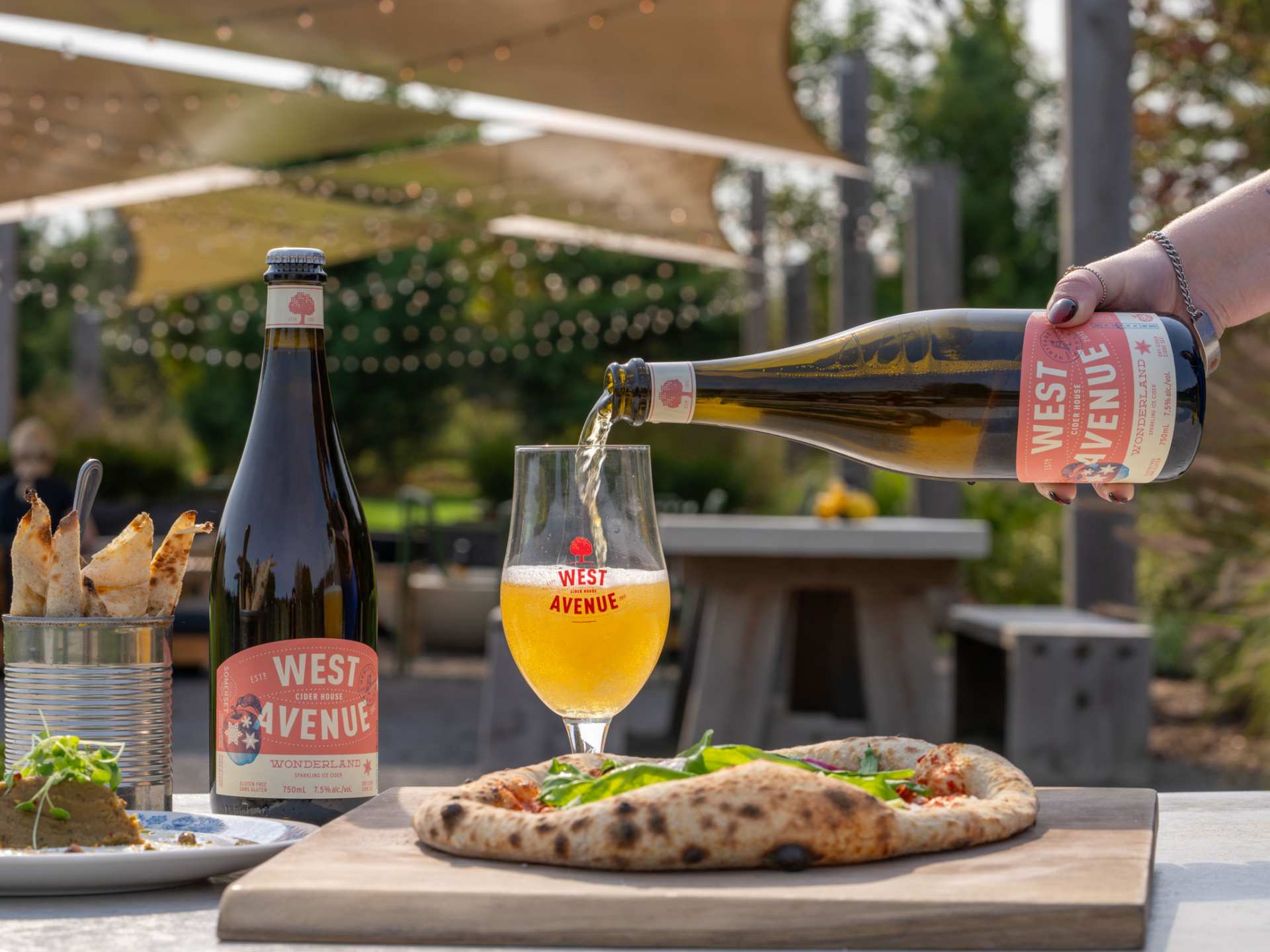 Support local with Feast On | A West Avenue Cider is poured in front of a pizza on a patio