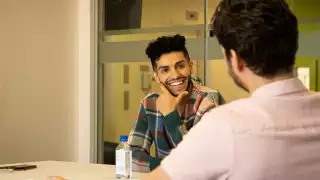 Mena Massoud | Aladdin actor Mena Massoud smiling and sitting at a table