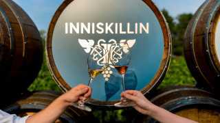 Two glasses of icewine clink in front of an Inniskillin barrel