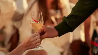 A glass of G. H. Mumm champagne is extended from one hand to another