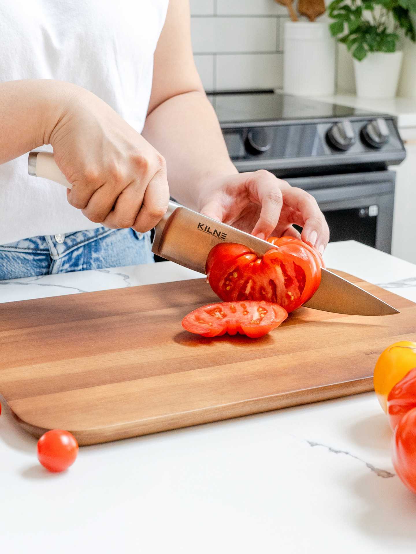 Kilne Ultimate Knife Set review | Person chopping a tomato on a cutting board with the Kilne Ultimate Knife Set chef's knife