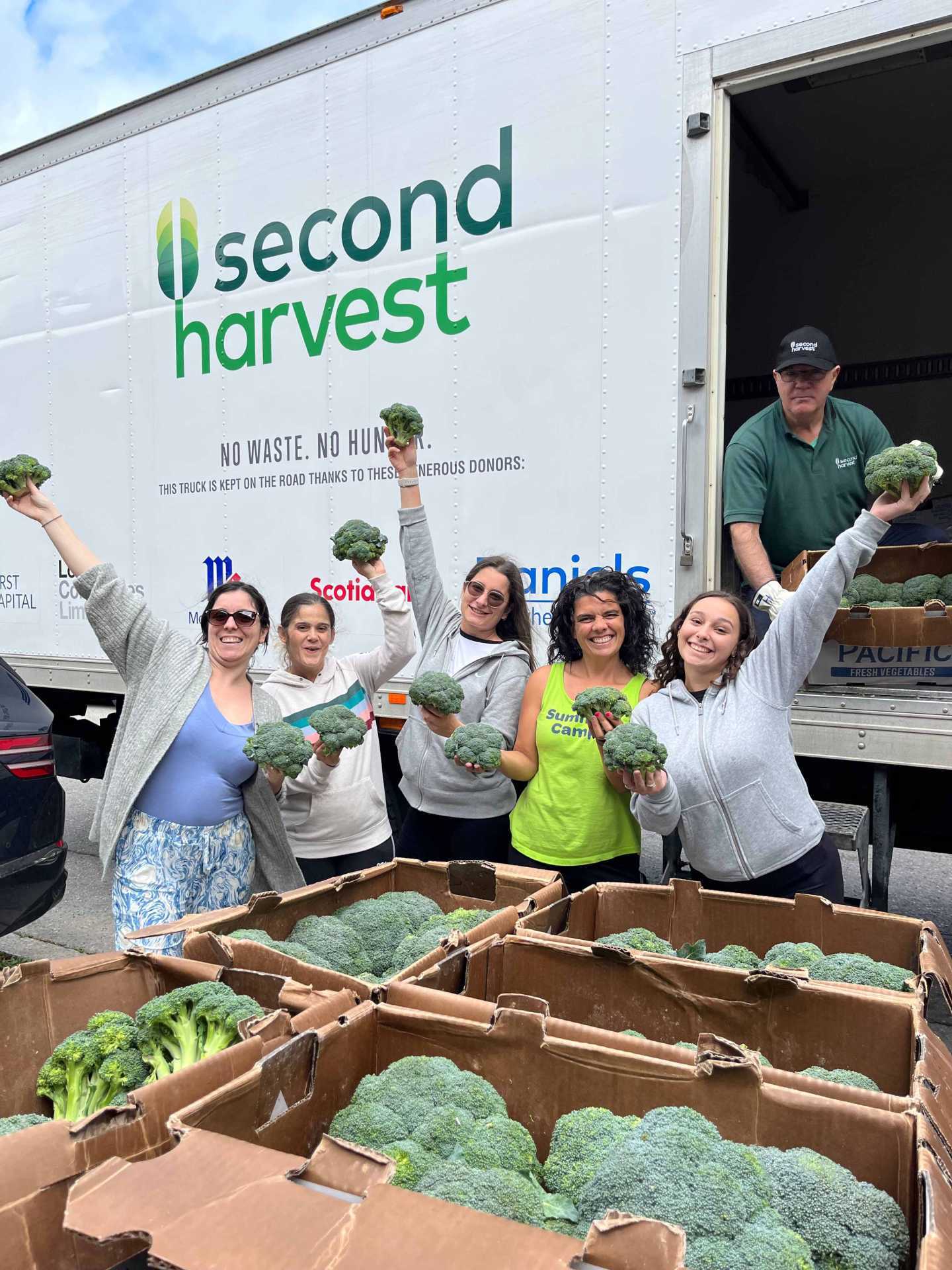 A group of Second Harvest volunteers holding broccoli in the air
