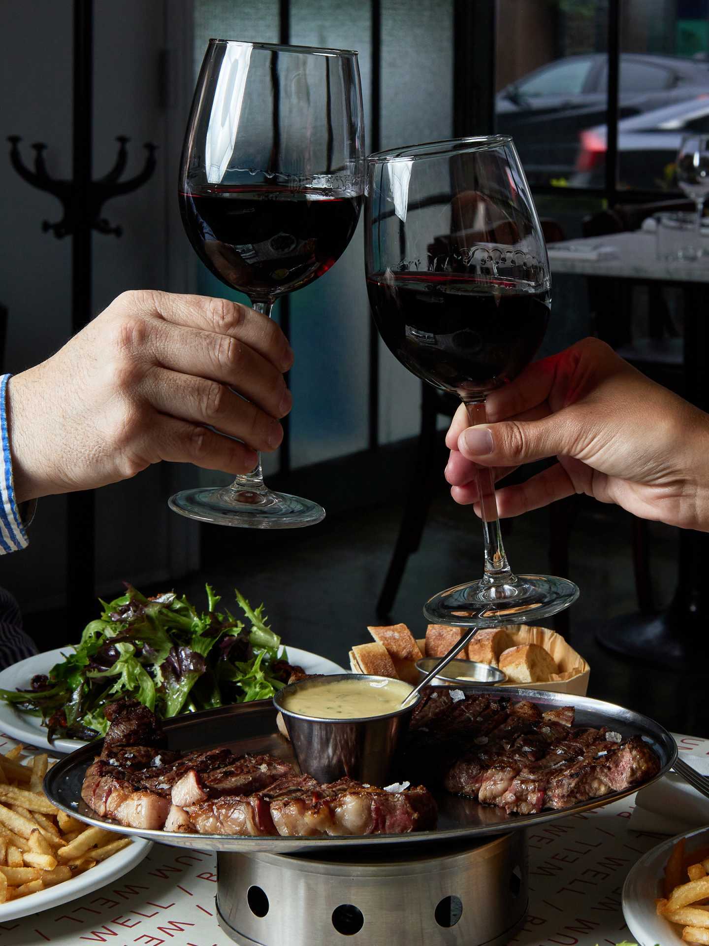 Best new Toronto restaurants | Two guests cheersing glasses of red wine at J's Steak Frites