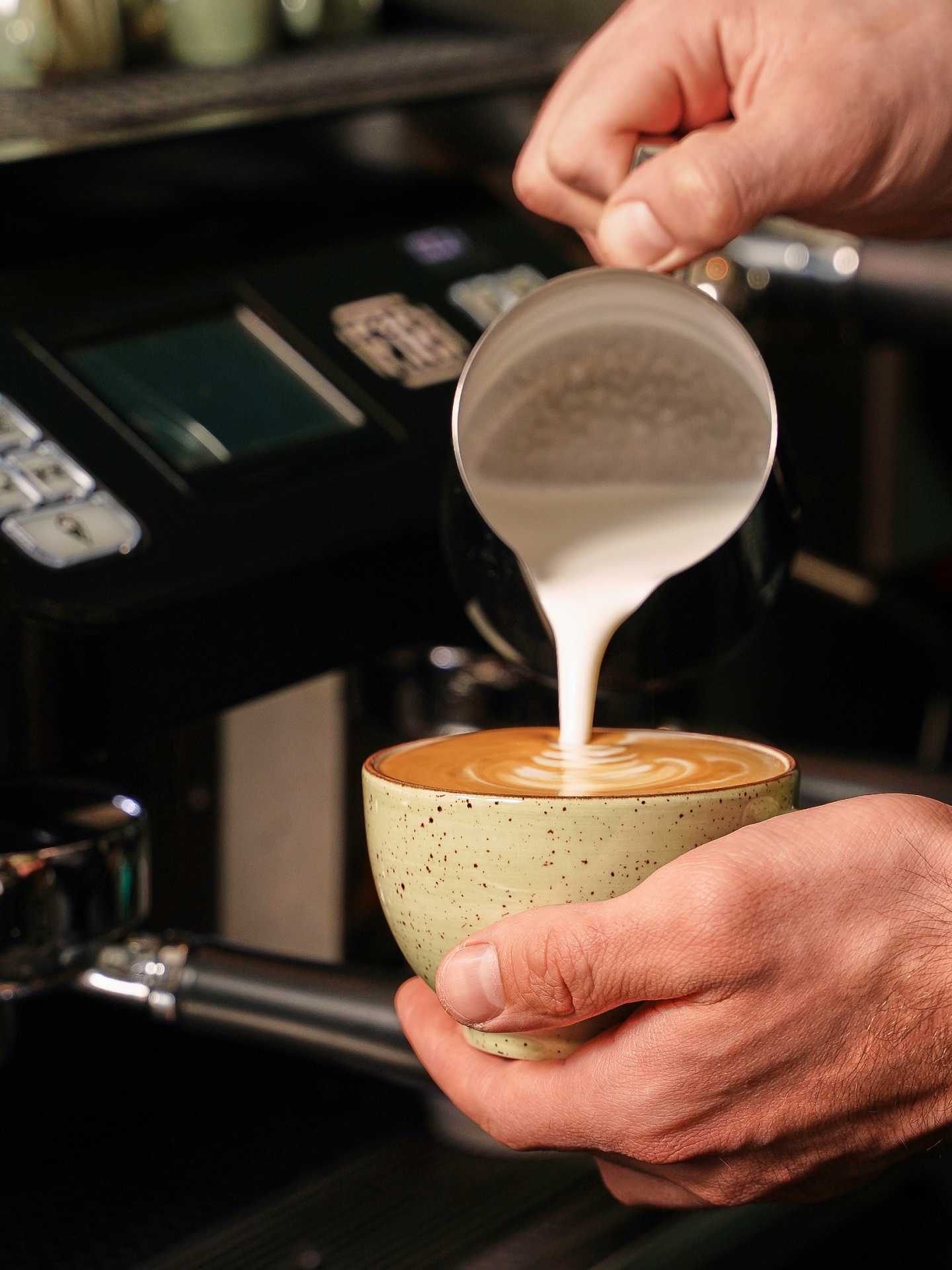 A barista pouring a cappuccino at 11:59 Bar:Café