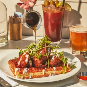 Maple syrup being poured on a stack of chicken and waffles at The Drake