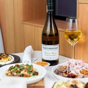 A bottle of white wine and a glass on a white tablecloth table with food