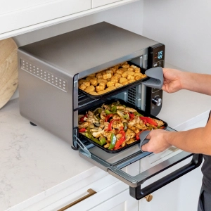 Someone pulling chicken nuggets and chicken and peppers out of the Ninja 12-in-1 Double Oven