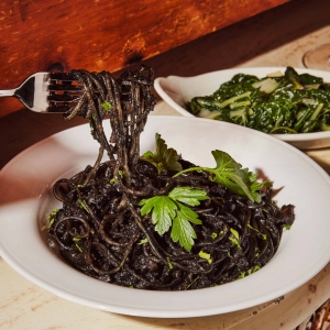 Joso's | A person holding a forkful of black squid ink spaghetti