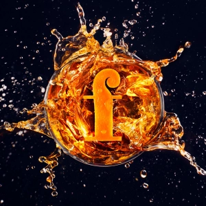 The Foodism F in a glass of orange liquid