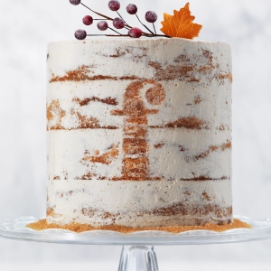 A tall white cake with berries and a maple leaf as garnish