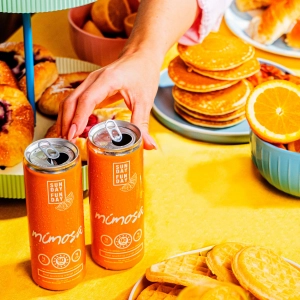 Two cans of Sunday Funday Mimosa with a brunch spread