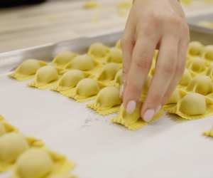 A hand places hand-rolled pasta on a baking tray