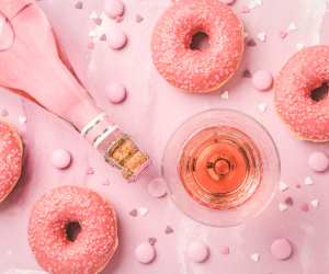 Overhead of a pink cocktail surrounded by doughnuts and a bottle of rosé